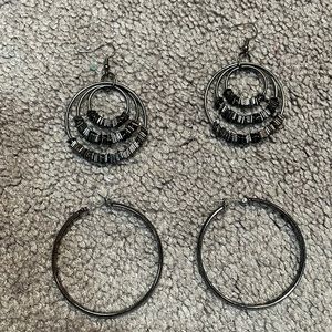 Two pair of gun metal colored hoop earrings.